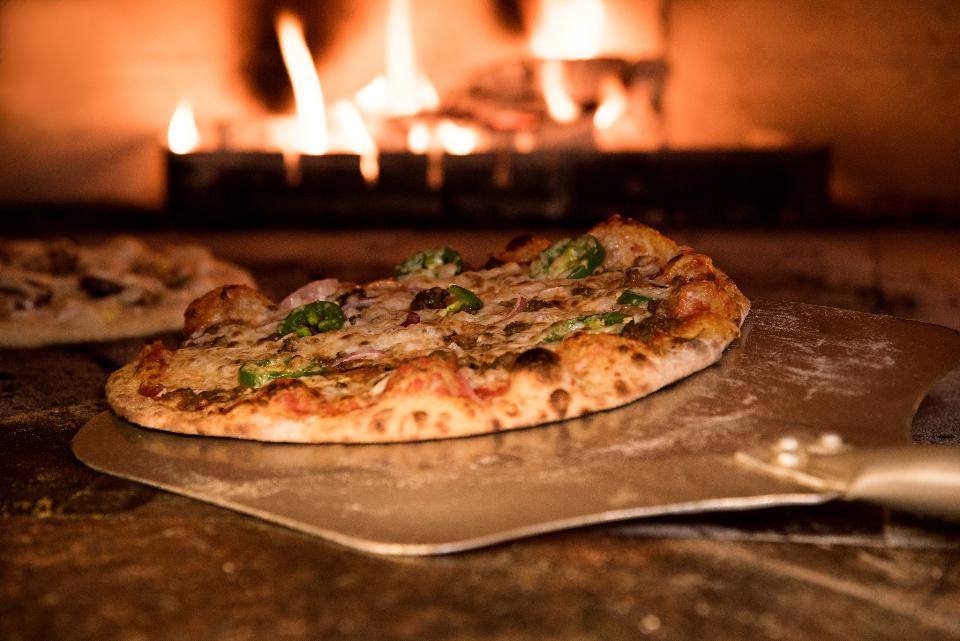 Pizza coming out of the wood fired oven on a metal peel